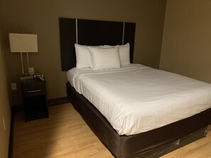 A neatly made bed with white linens, a dark headboard, and a bedside table with a lamp and a clock. - Pitkin Hotel (Brooklyn)