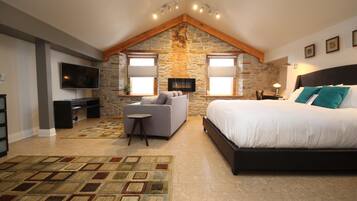 A bedroom with a stone wall, a bed, a TV, a sofa, and a small table.