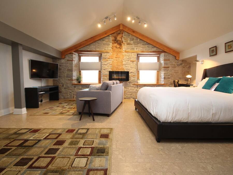 A bedroom with a stone wall, a bed, a TV, a sofa, and a small table.