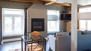 A living room with a glass table, a grey sofa, a fireplace, and a TV mounted on a stone wall. - Arrow Properties (North Grenville)