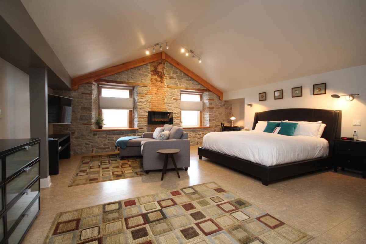A bedroom with a stone wall, a bed, a sofa, a TV, and a fireplace.