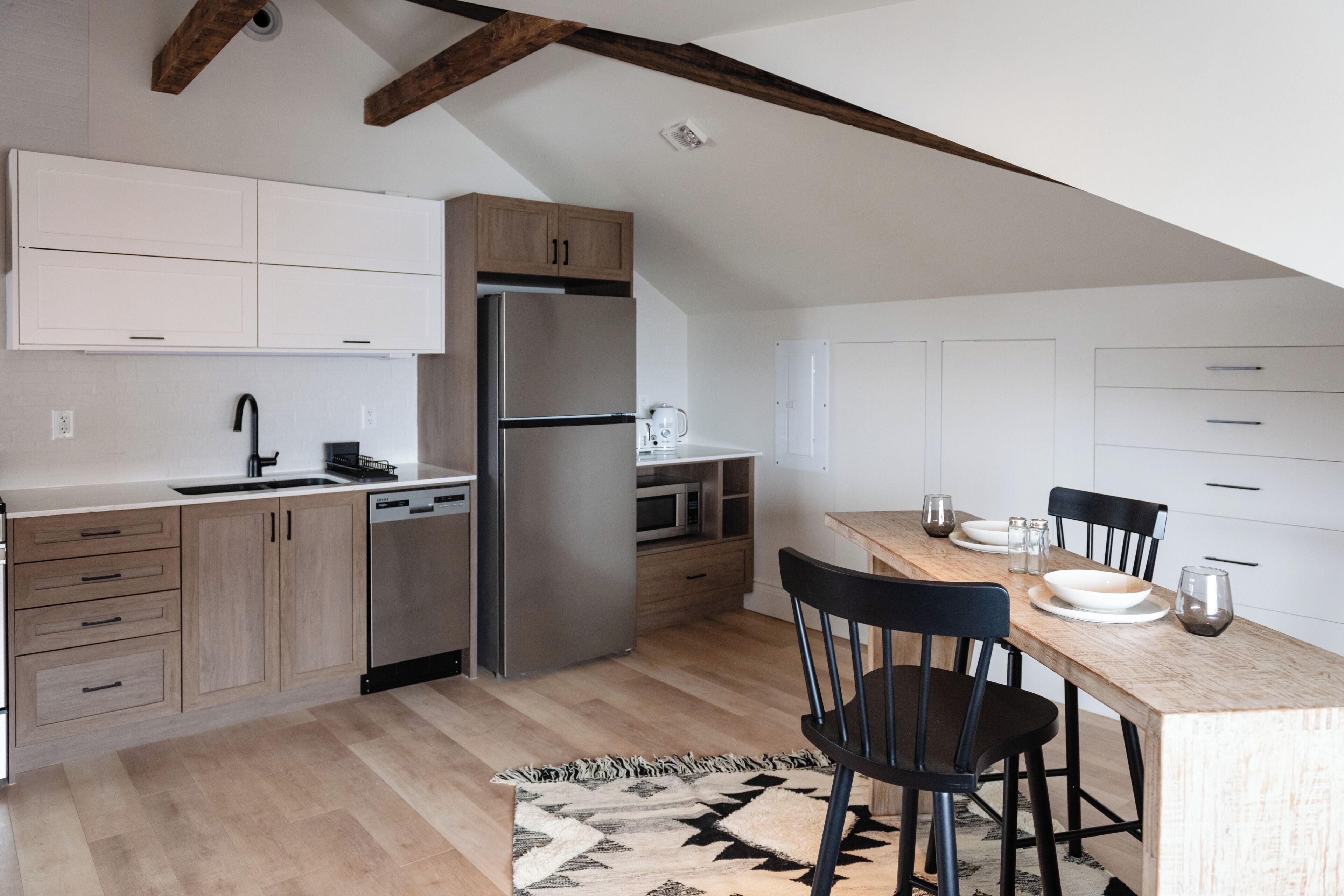 Une cuisine moderne avec des meubles en bois, un réfrigérateur en acier inoxydable et un coin repas comprenant une table et des chaises en bois.