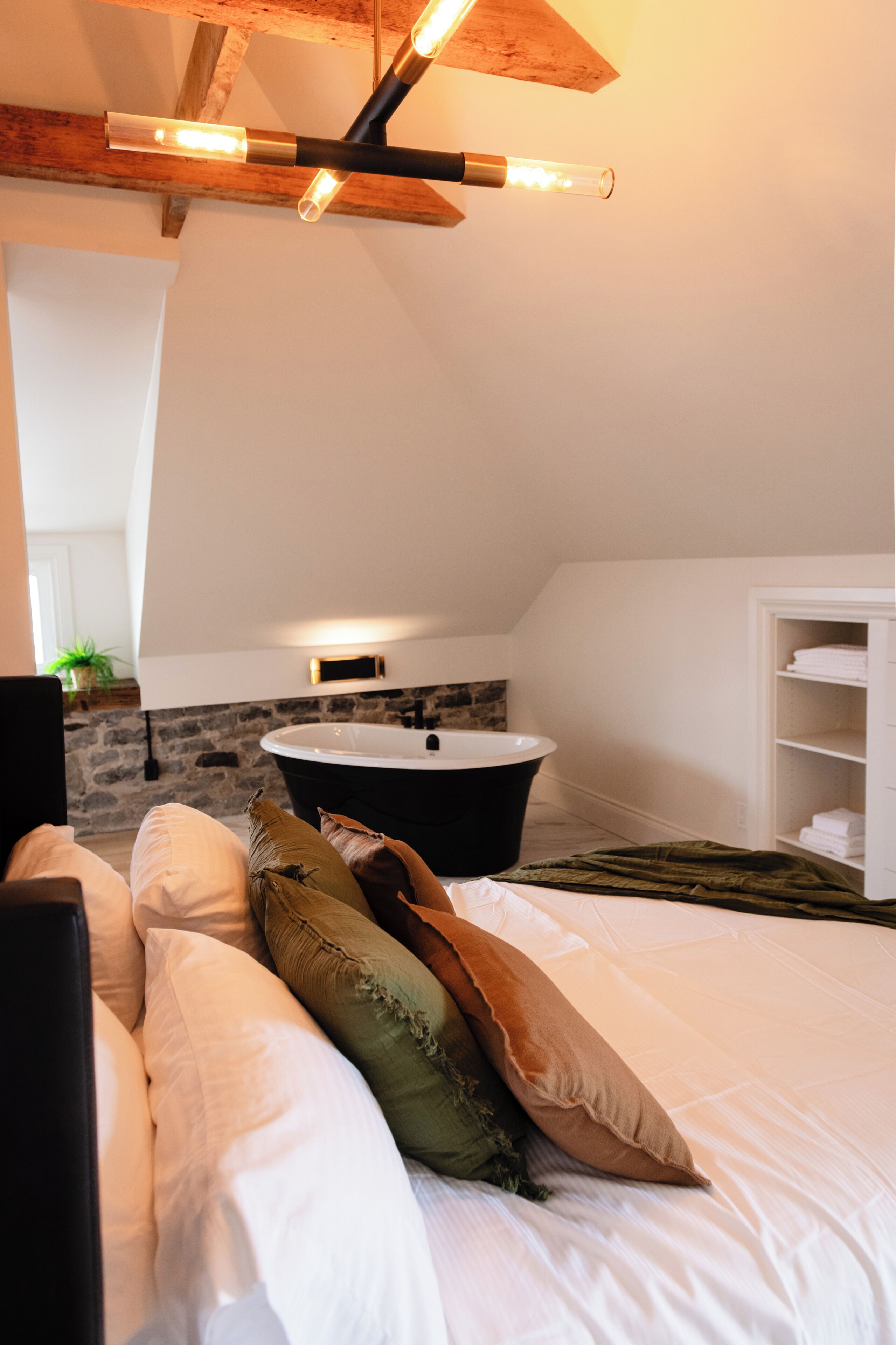 A bedroom with a bed, pillows, a bathtub, and a white wardrobe.