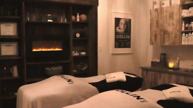A spa room with two beds, a fireplace, shelves with various items, and a poster on the wall. - Arrow Properties (North Grenville)