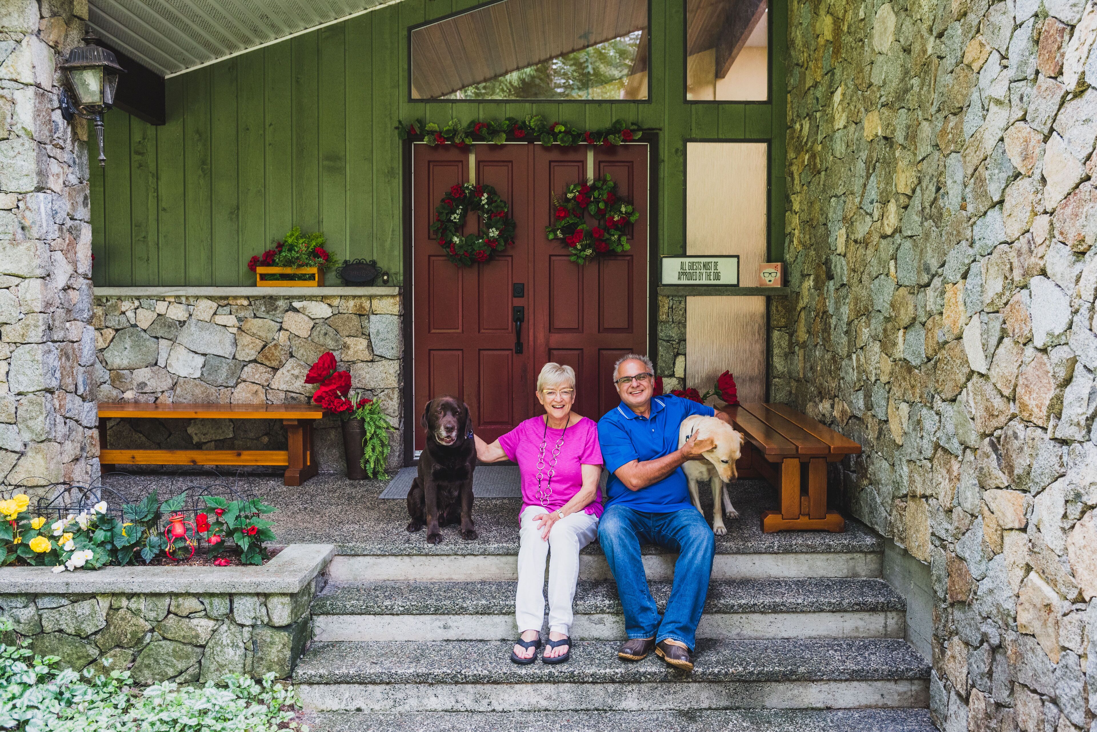 A stone wall, wooden steps, a bench, a wooden door with wreaths, and a sign.