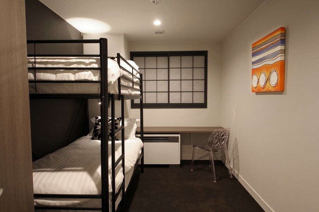 A dormitory room with bunk beds, a desk, and a chair.