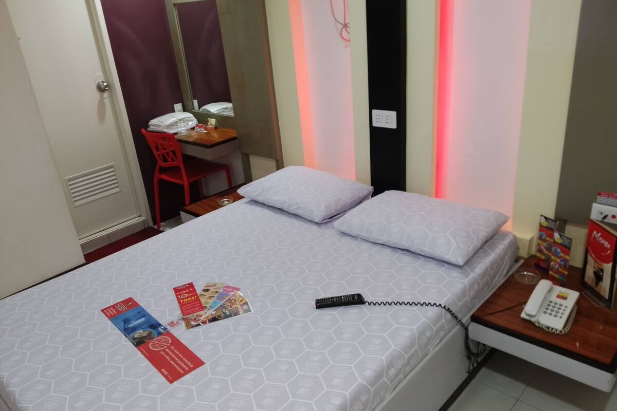 Una habitación de hotel con cama, escritorio con silla, teléfono y atril para menú.