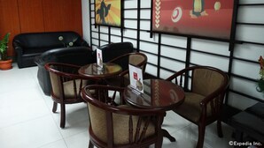 A hotel lobby with a black leather sofa, wooden chairs, a glass table, and artwork on the walls. - Hotel Sogo EDSA Harrison (Pasay)
