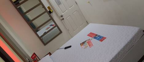 A hotel room with a bed, a TV mounted on the wall, a door with a lock, and a mirror on the wall.