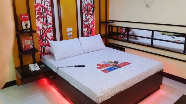 A hotel room with a bed, a bedside phone, a red light strip, a shelf with a phone and a magazine, and a wall-mounted air conditioner. - Hotel Sogo EDSA Harrison (Pasay)