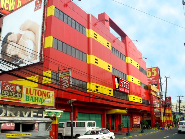Un edificio de varios pisos con una fachada llamativa en rojo y amarillo, que muestra un letrero del Hotel 500 Grand y una cafetería con acceso directo desde el coche.