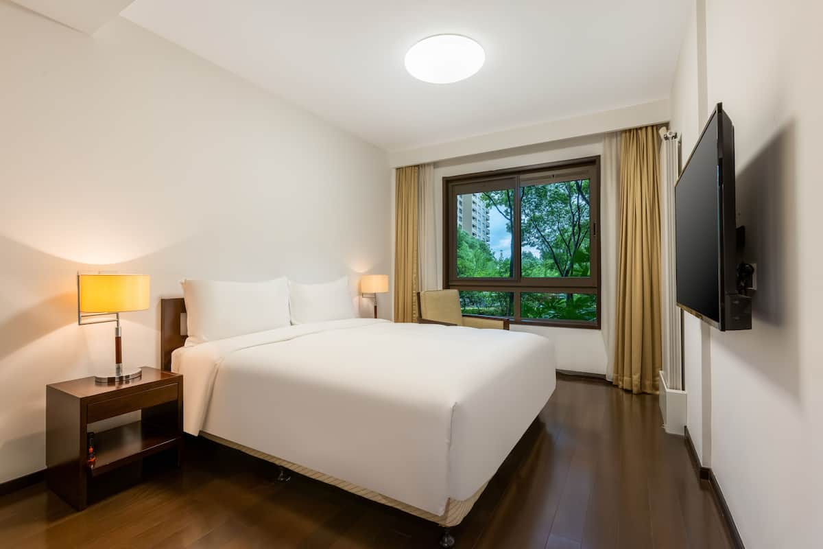 Een hotelkamer met een groot bed, een nachtkastje met een lamp, een aan de muur bevestigde televisie en een raam met gordijnen.