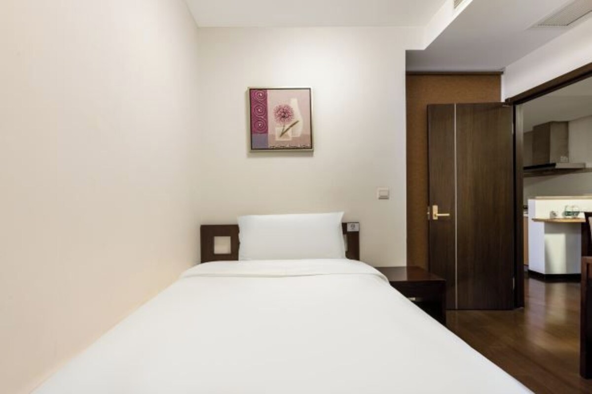 Une chambre d’hôtel comprenant un lit, une table de chevet, une œuvre d’art accrochée au mur et une porte donnant sur une petite cuisine.