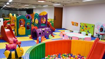 Un área de juegos infantiles con estructuras de juego coloridas, una piscina de pelotas y pequeñas mesas y sillas.