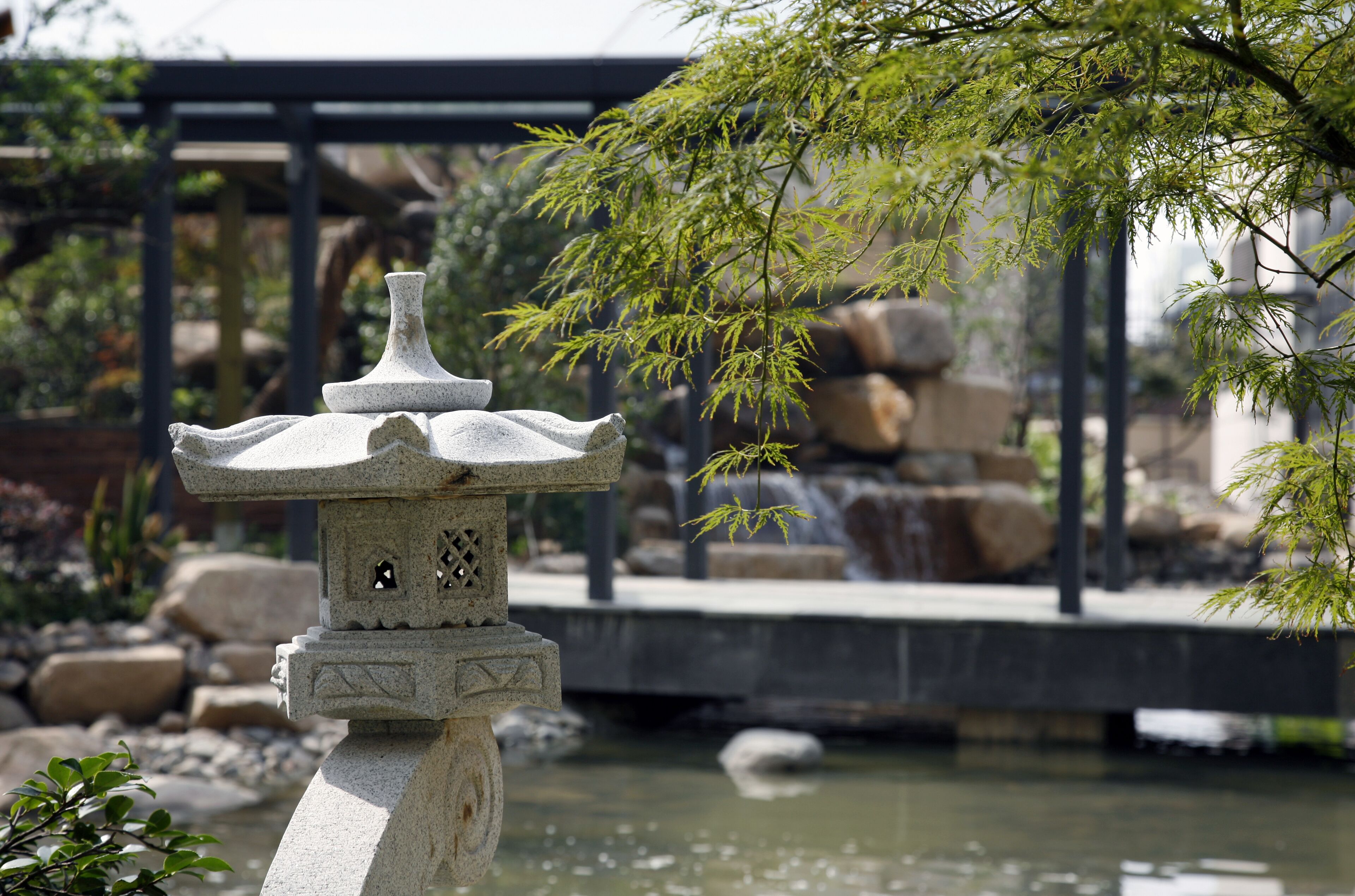 A stone lantern in a garden with a bridge and rocks in the background.