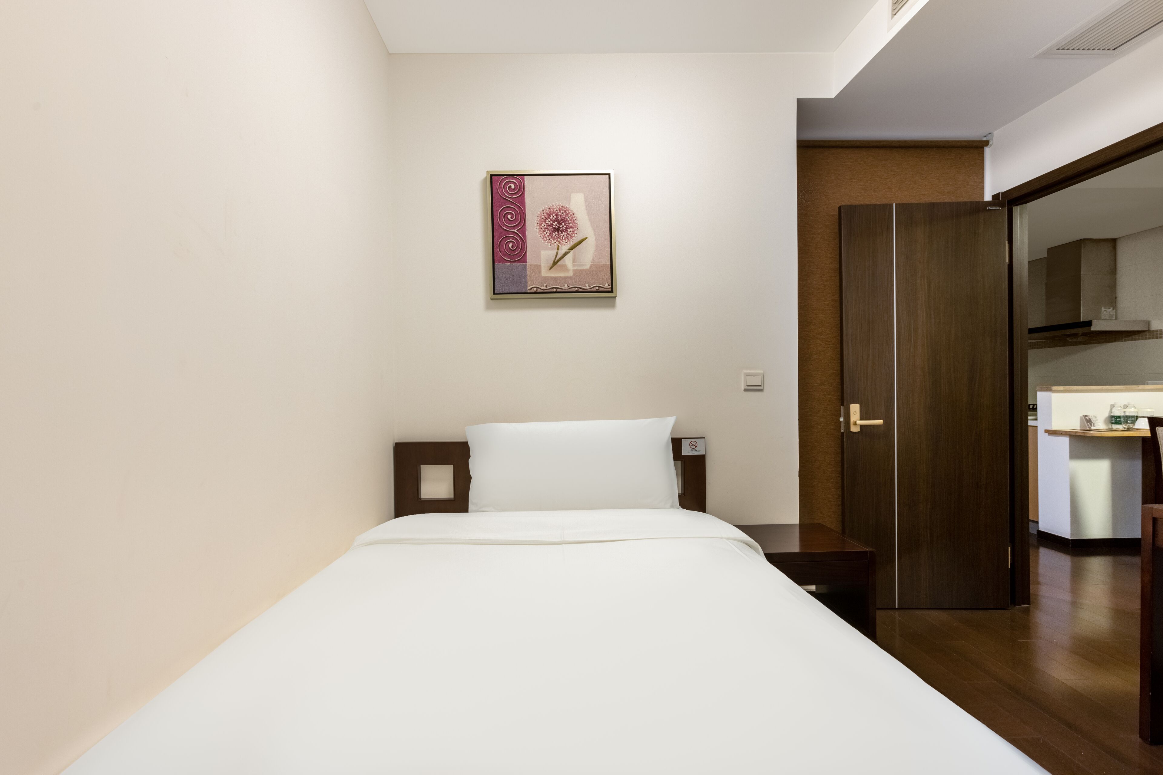 Habitación de hotel con cama, mesita de noche, una obra de arte colgada en la pared, una puerta y una zona de kitchenette.
