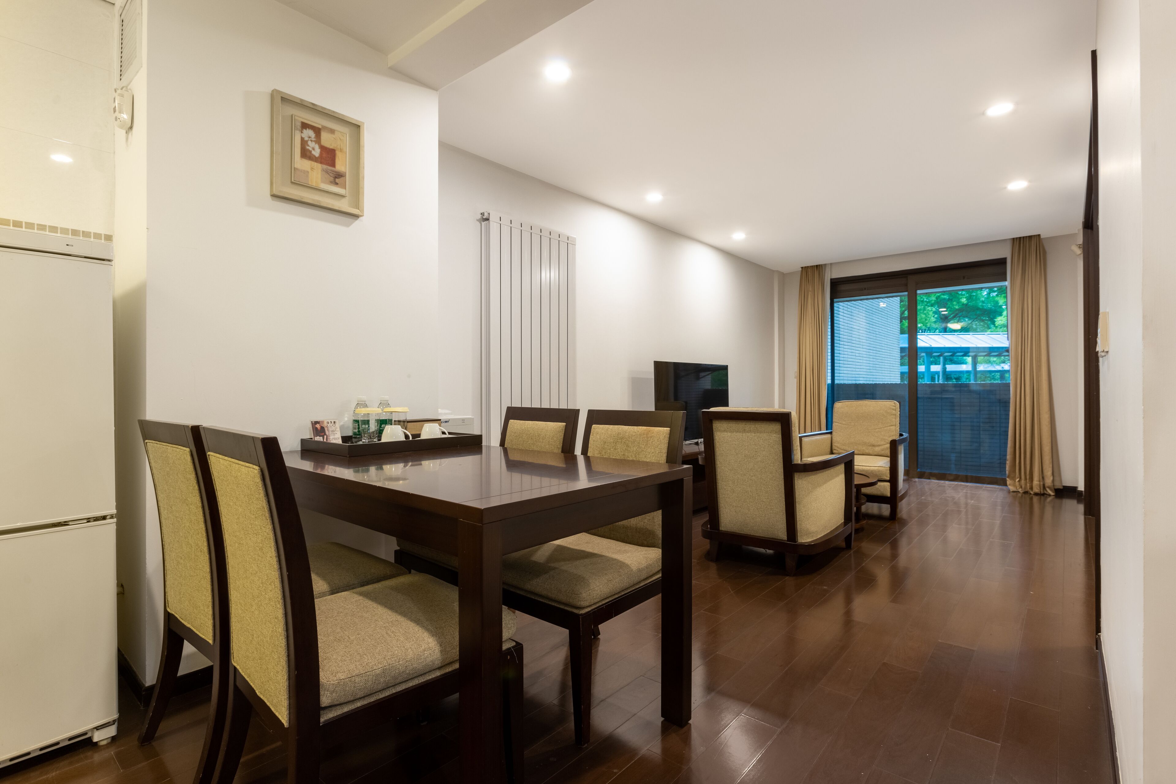 A dining area with a wooden table and chairs, a refrigerator, a TV, and a window with curtains.