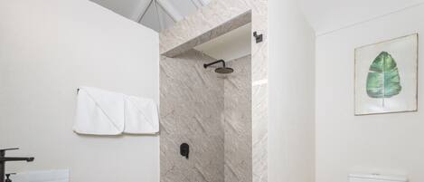 A bathroom with a marble sink, a black bowl, a shower with a marble wall, a white toilet, and a framed leaf on the wall.