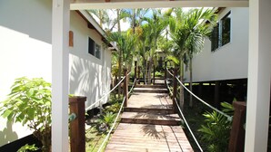 A wooden pathway leading to a white building with multiple windows, surrounded by lush greenery and palm trees. - Muri Lagoon View Bungalows (Rarotonga)