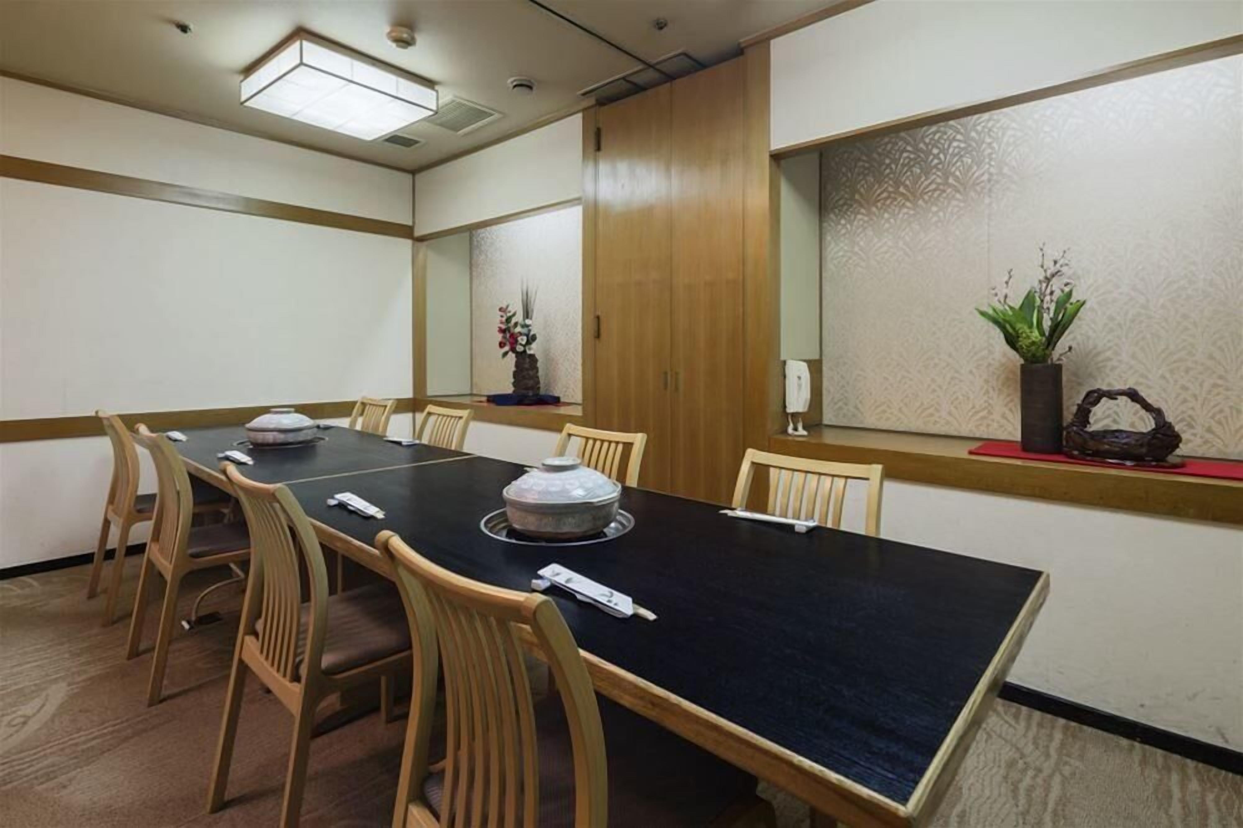A conference room with a long table, wooden chairs, and a decorative vase on the windowsill.