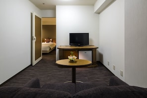 Ein Hotelzimmer mit einem Bett, einem Fernseher auf einem Schrank, einem kleinen Tisch mit einer Vase und einem Sofa.