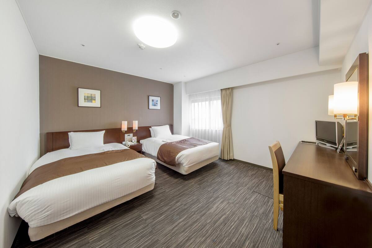 A hotel room with two beds, a desk, and a television.
