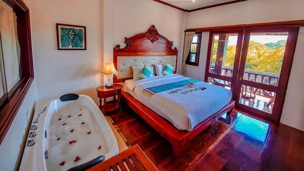 A bedroom with a large bed, a bathtub, and a balcony with a view. - The View Pavilion (Luang Prabang)