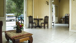 A hotel lobby with a tiled floor, a wooden table with a vase of flowers, two chairs, and a view of the outside through a glass door. - The View Pavilion (Luang Prabang)