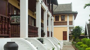 A traditional building with a stone pathway, white columns, and a wooden balcony. - The View Pavilion (Luang Prabang)