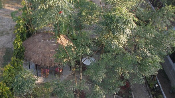 A thatched-roof structure with a circular design, surrounded by dense greenery and a gravel path. - Hotel Park Inn (Sauraha)