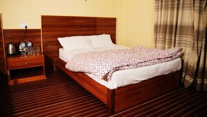A wooden bed with white bedding, a nightstand with a kettle and glasses, and a striped curtain. - Hotel Park Inn (Sauraha)
