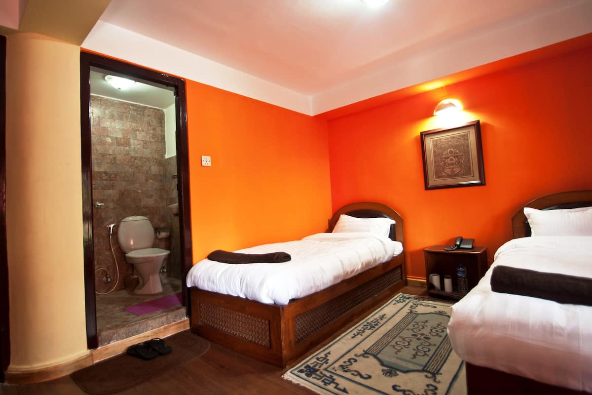 Habitación de hotel con cama de madera, una mesita de noche pequeña, baño con cabina de ducha de vidrio y un aplique de pared.