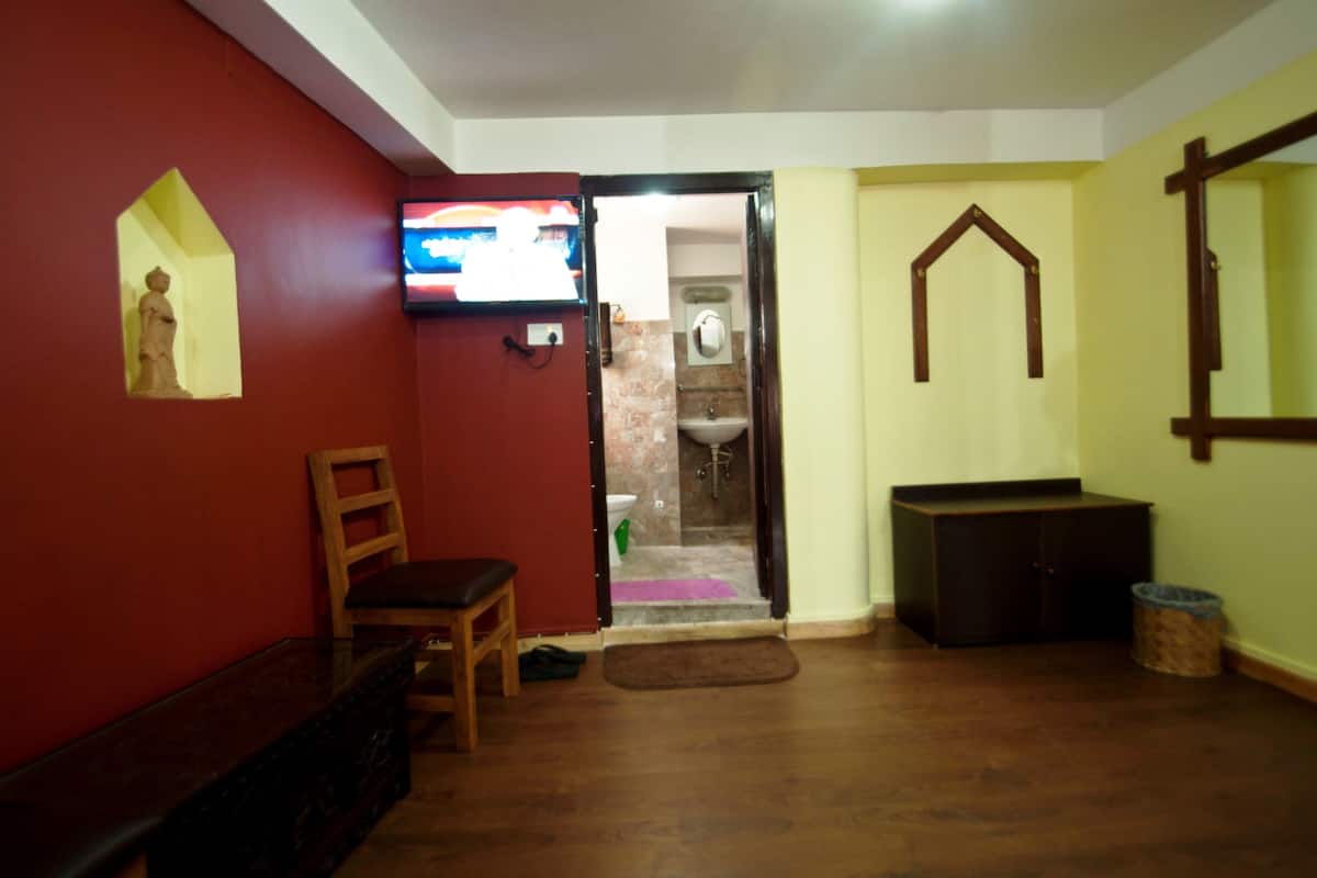 Una habitación con banca de madera, televisor, baño con ducha y un armario.