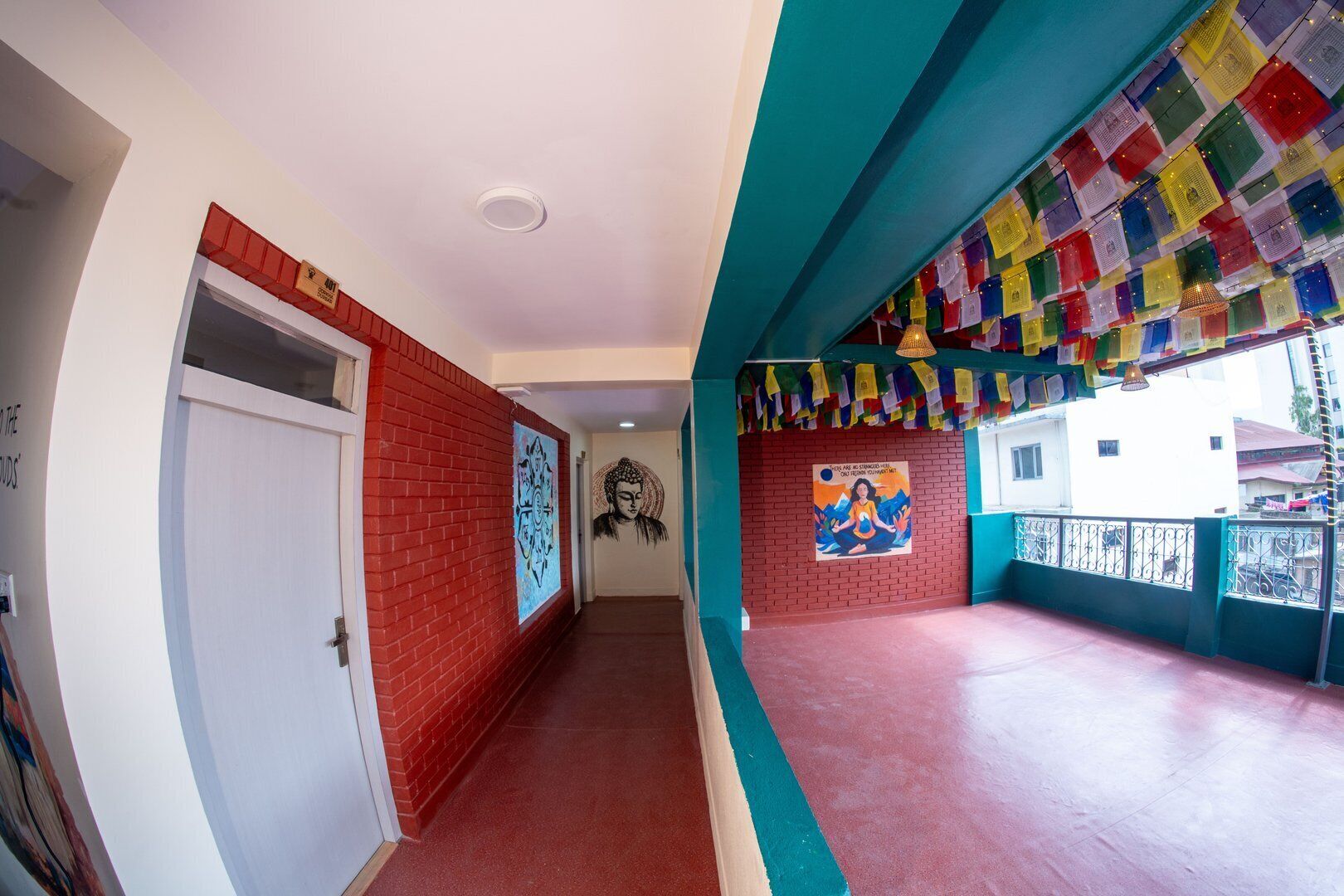 A corridor with red brick walls, a white door, and a mural. There is a poster with a meditative figure and text. The ceiling is white, and the floor is red.