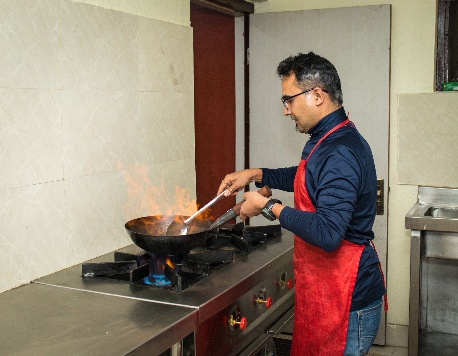 A person cooking in a kitchen with a wok on a stove.