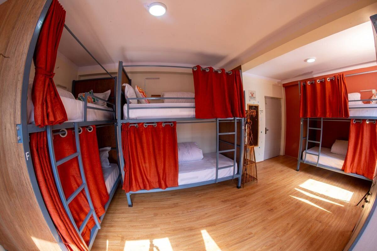 A bunk room with three bunk beds, red curtains, and a wooden floor.
