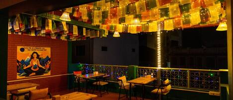An outdoor seating area with tables and chairs, decorated with colorful lights and a mural on the wall.