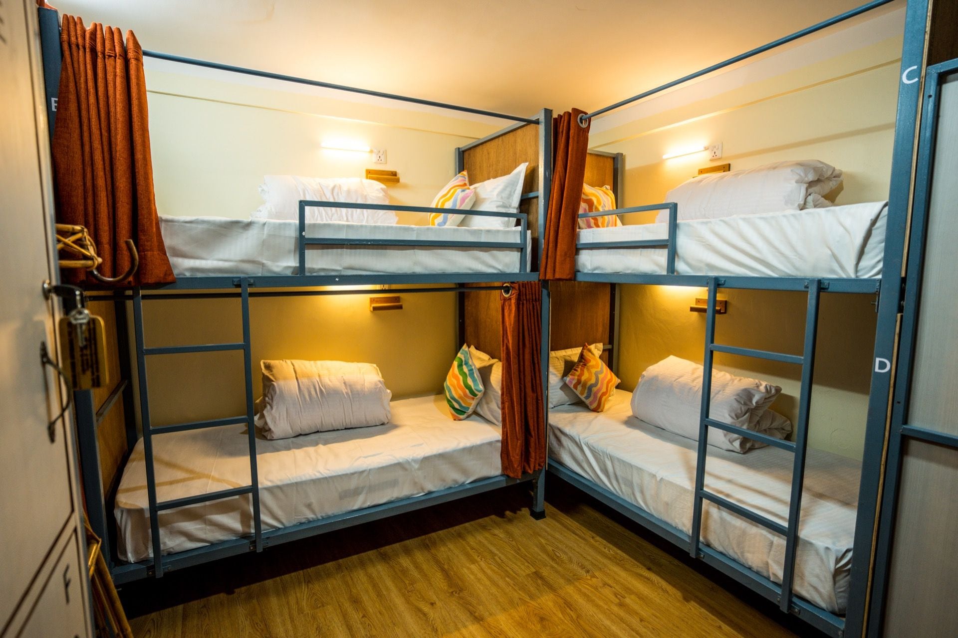 Habitación con literas de metal, piso de madera y una cortina.