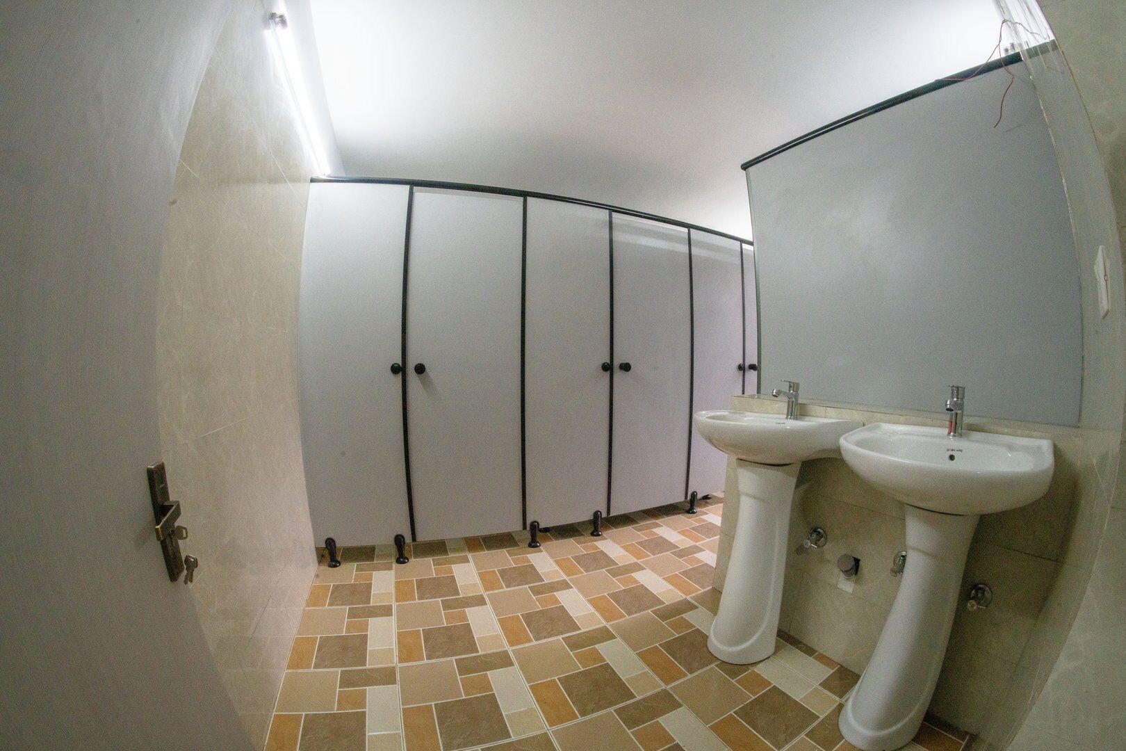 A bathroom with a tiled floor, a sink, a mirror, and a row of lockers.