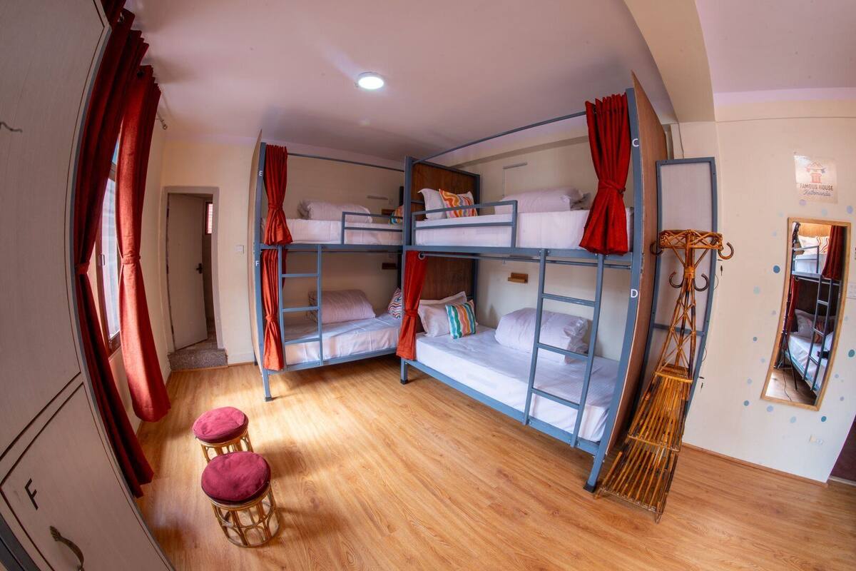 A dormitory room with bunk beds, a wooden floor, a mirror, and a small stool.