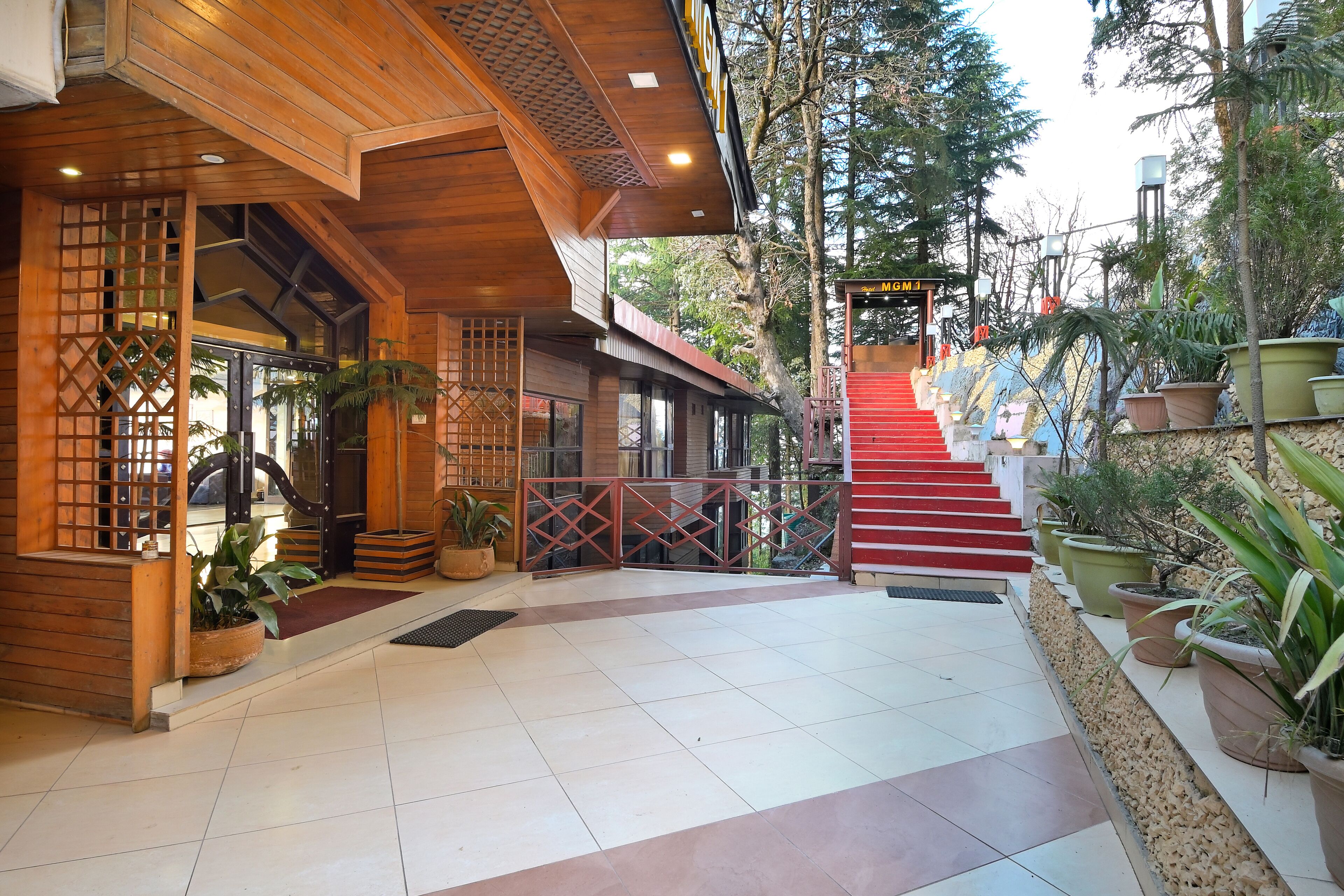 A wooden building with a staircase leading to a red door, surrounded by potted plants.