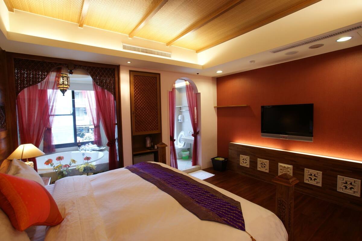 A hotel room with a bed, a TV mounted on the wall, and a window with curtains.
