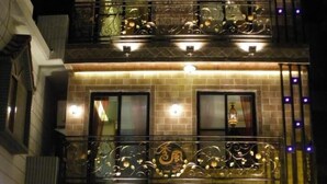 Un edificio de varios pisos con una recepción en la planta baja, un balcón con barandillas decorativas y una unidad de aire acondicionado visible.