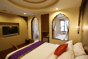 Una habitación de hotel con una cama grande, televisión, una mesita y una silla.