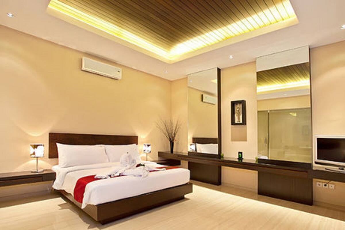 A modern hotel room with a large bed, a TV, a mirror, and a bedside table.