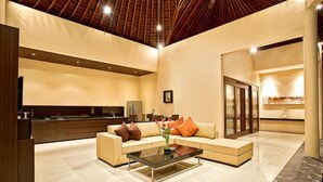 A spacious living area with a high ceiling, a sofa set, a coffee table, and a kitchen in the background. - Arsa Villa Bali (Seminyak)