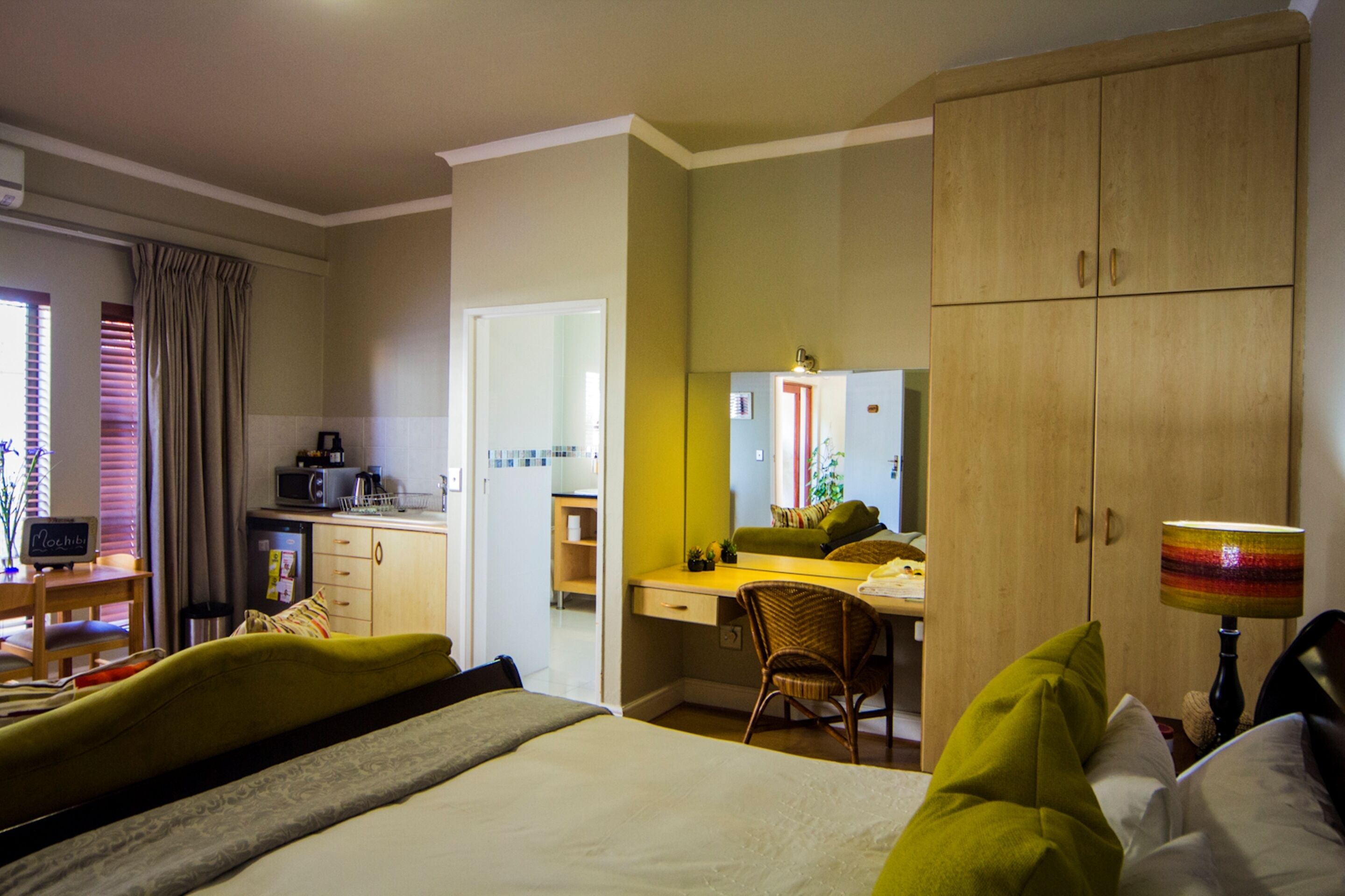 A hotel room with a bed, a desk, a chair, a wardrobe, and a small kitchenette.