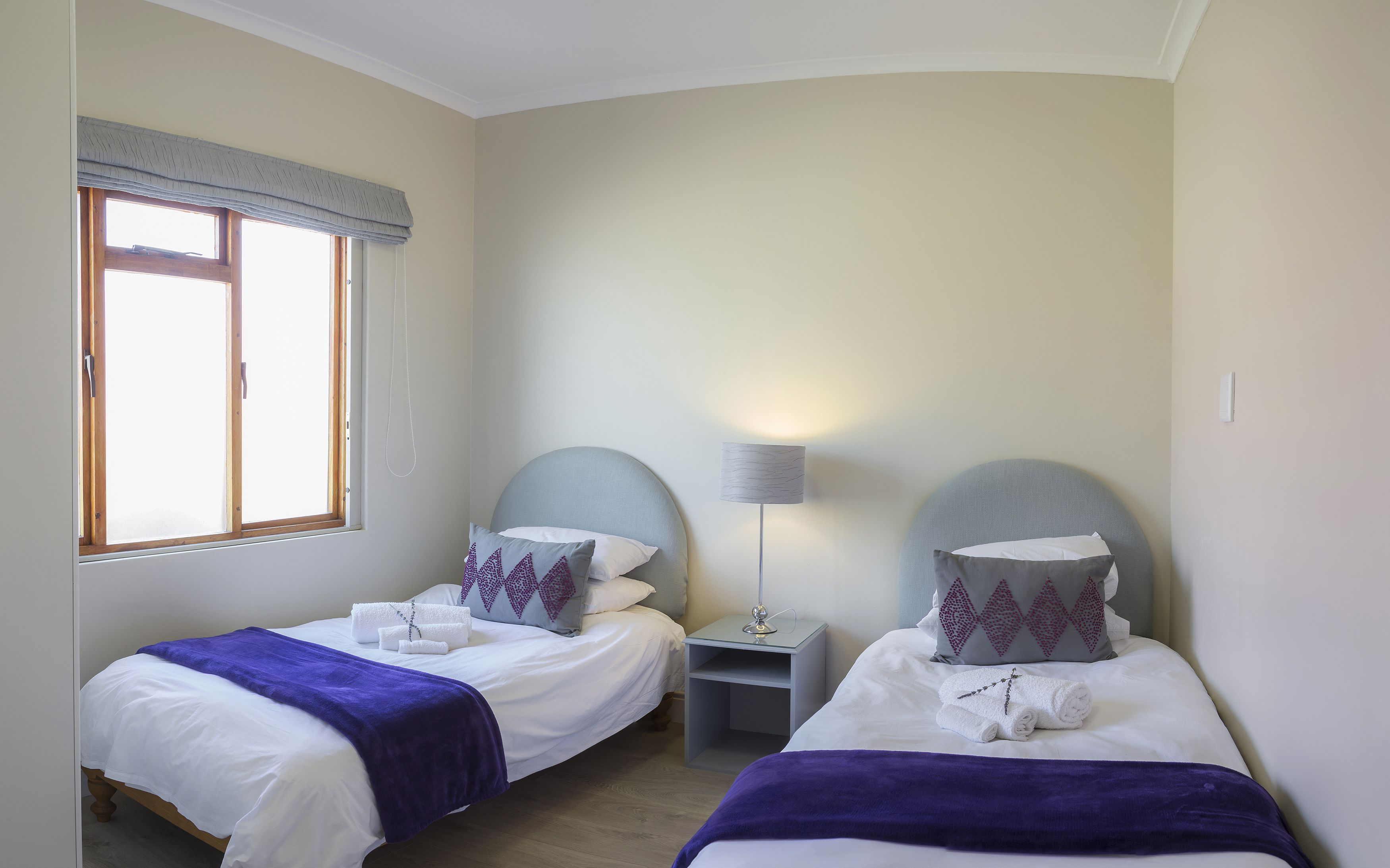 A hotel room with two single beds, each with a headboard, a bedside table, and a lamp.
