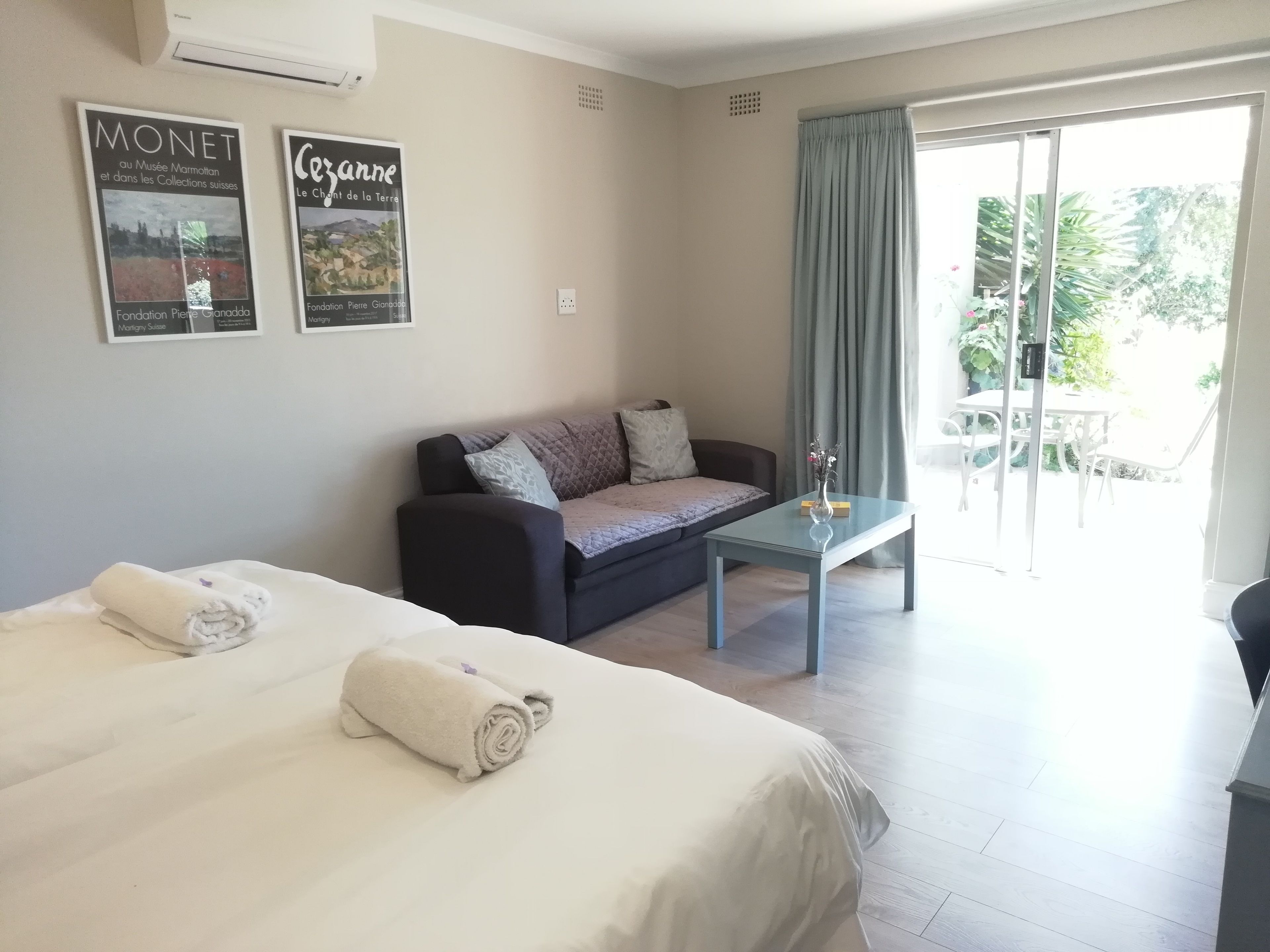Hotelkamer met twee bedden, een slaapbank, een tafel met glazen blad en uitzicht op de omgeving.
