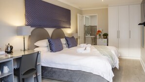 Ett hotellrum med en säng, ett skrivbord med en stol, en lampa, en kaffebryggare och en garderob.
